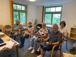 Ein Mann und vier Frauen sitzen nebeneinander auf St&uuml;hlen und blicken zur Seite in die Kamera.