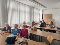 F&uuml;nf Damen und drei Herren sitzen an drei Tischen im Raum und blicken nach Vorne in die Kamera.