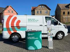 Das Info-Mobil des Digitalen Engel steht mit dem Info-Stand auf einem Parkplatz in Sandersdorf. Im Hintergrund stehen H&auml;user.