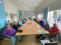 &Uuml;ber zwanzig Senior:innen sitzen an einem gro&szlig;en langen Tisch in einem Veranstaltungsraum des Nachbarschaftstreff West.