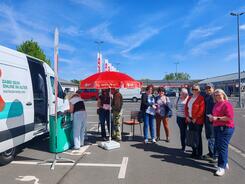 Eine Gruppe von Frauen und M&auml;nnern steht vor dem Infomobil und blickt in die Kamera.