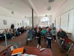 Im Stadthaus in Hessisch Oldendorf (ein gro&szlig;er Raum) sitzen auf mehreren Stuhlreihen und an der Seite Menschen zwischen 50 und 90 Jahren.