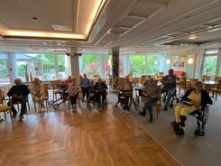 In einem gro&szlig;en Raum sitzen auf Tischen oder Rollatoren knapp zehn Senior:innen. Sie sind schlecht zu erkennen, weil das Bild relativ dunkel ist.