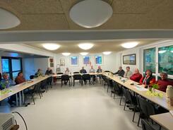 Im Weitwinkel-Format sitzen in U-Form an Tischen ca. 13 Personen. 
