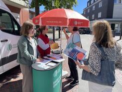 Theresa und eine Mitarbeiterin der Caritas beraten zwei &auml;ltere Damen am Infostand.
