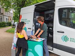 Eine Dame steht vor dem Infomobil und blickt zusammen mit Referent Johannes auf einen Laptop.