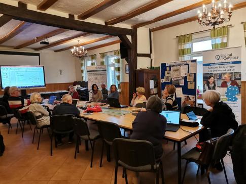 Personen sitzen an einem gro&szlig;en Tisch vor mitgebrachten Laptops
