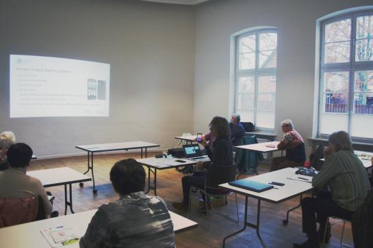 Die Teilnehmenden sitzen im Raum und schauen zur Pr&auml;sentation an der Wand