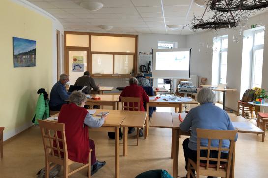 Senioren in Barnstorf sitzen an Tischen und schauen auf Leinwand