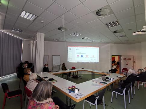 Die Teilnehmenden sitzen im Raum und schauen zur Pr&auml;sentation an der Wand