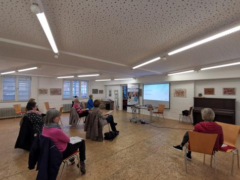 Die Teilnehmenden sitzen im Raum und schauen zur Pr&auml;sentation an der Wand