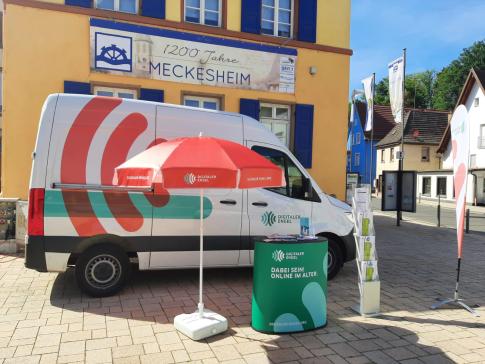 Der Info-Stand mit dem Info-Mobil steht auf dem Rathausvorplatz in Meckesheim. Dahinter ist ein Schild mit der Aufschrift "1200 Jahre Meckesheim" aufgeh&auml;ngt.