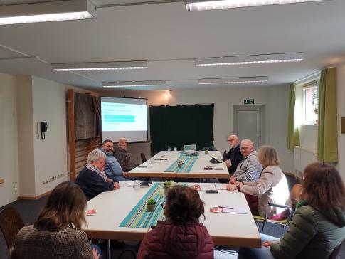 Die Teilnehmenden sitzen im Raum und schauen zur Pr&auml;sentation an der Wand
