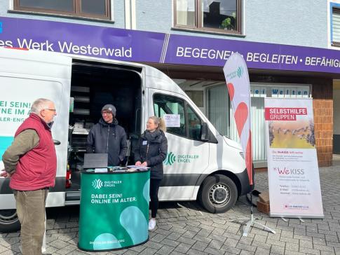 Ein Besucher steht vor dem Infomobil und unterh&auml;lt sich mit unserem Referenten Johannes und Vanessa Hastrich von der WeKISS