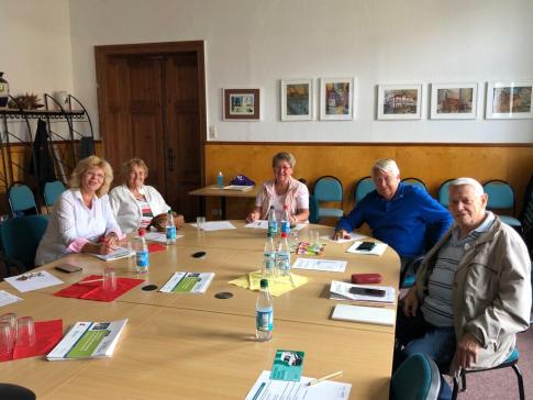 Die Ansprechpartnerin der Stadtbibliothek sitzt mit vier Senior:innen an einem runden Tisch. Auf dem Tisch liegen Smartphones und Brosch&uuml;ren.