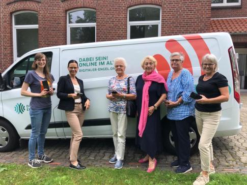 Petra steht mit f&uuml;nf Seniorinnen vor dem Info-Mobil. Alle halten ein Smartphone in der Hand und gucken in die Kamera.