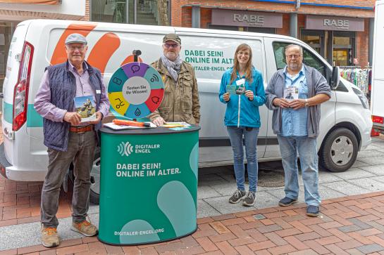 Petra steht mit Peter Aldag, Manfred Grimm und Hein K&ouml;hler am Info-Stand vor dem Info-Mobil. Alle vier posieren in die Kamera.