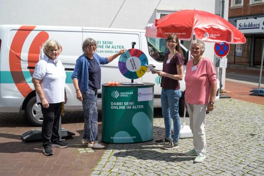 Drei Mitglieder des SeniorInnenbeirats Harsefeld stehen mit Petra am Info-Stand vor dem Info-Mobil und l&auml;cheln in die Kamera.