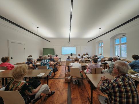 Die Teilnehmenden sitzen im Raum und schauen zur Pr&auml;sentation an der Wand