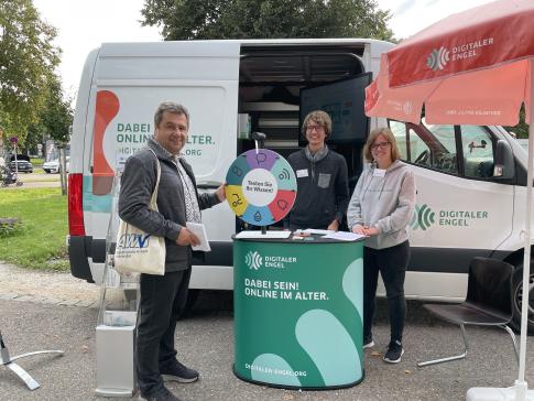 Johannes, Theresa und ein Besucher, der am Gl&uuml;cksrad dreht, l&auml;cheln in die Kamera.