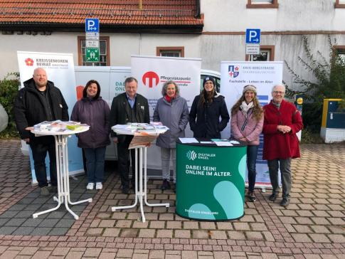 Am Info-Stand gehen gemeinsam sieben Personen der beteiligten Organisationen. In der Mitte steht der B&uuml;rgermeister. 