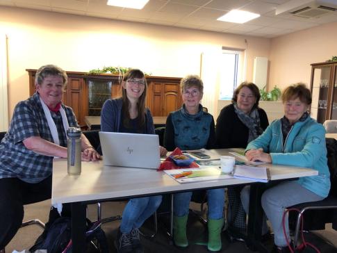 Petra sitzt mit vier Seniorinnen an einem Tisch auf dem ein Laptop steht. Alle f&uuml;nf Personen schauen und l&auml;cheln in die Kamera.