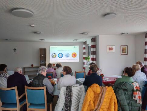Die Teilnehmenden sitzen im Raum und schauen zur Pr&auml;sentation an der Leinwand