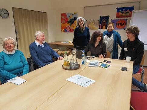 Einige Besucher:innen der Veranstaltung sitzen und stehen um einen gro&szlig;en Tisch herum 