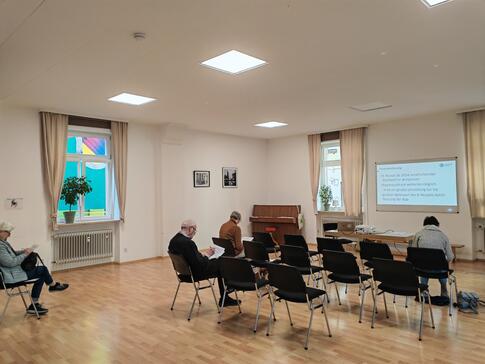 Die Teilnehmenden sitzen im Raum und schauen zur Pr&auml;sentation an der Leinwand