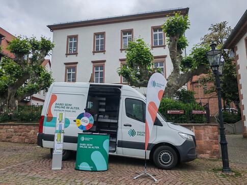 Das Infomobil steht mit Beachflag, Prospektst&auml;nder und Gl&uuml;cksrad vor einem Haus
