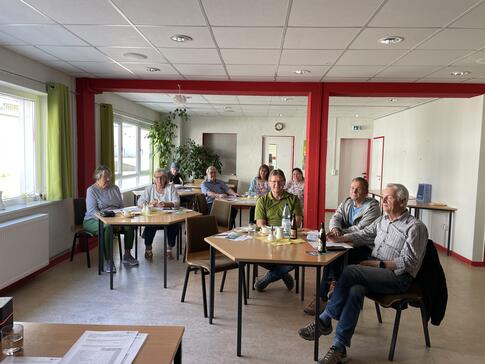 Die acht Teilnehmenden sitzen an drei Gruppentischen und l&auml;cheln in die Kamera.
