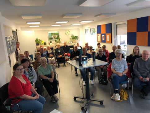 Ein Foto vom Veranstaltungsraum im Senioren- und Pflegest&uuml;tzpunkt Burgdorf. In der Mitte steht ein Beamer. Darum herum sitzen knapp 35 Senior:innen auf St&uuml;hlen, die nach vorne blicken.