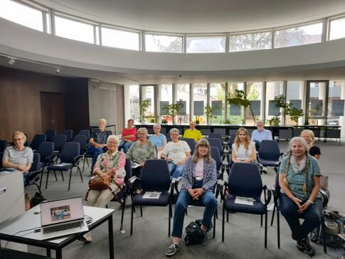 Ungef&auml;hr 12 Seniorinnen und 3 Senioren sitzen im Kollegiumssaal im Rathaus Elmshorn auf St&uuml;hlen und blicken nach vorne. Im Bild links vorne ist Petras Laptop zu sehen.