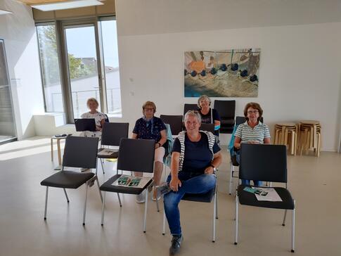 Kooperationspartner Frauke D&uuml;&szlig;mann und vier Seniorinnen sitzen auf St&uuml;hlen und gucken in die Kamera.