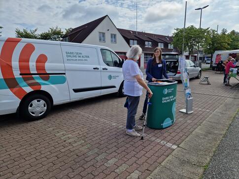 Petra steht mit einer Dame aus B&uuml;sum am Info-Stand vor dem Info-Mobil. Die beiden unterhalten sich. 