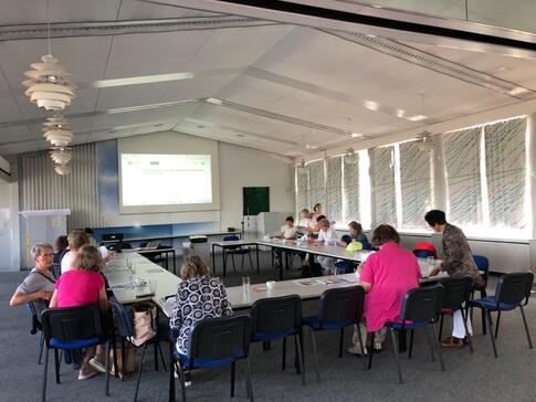 In einem gro&szlig;en Veranstaltungssaal im Neuen Kieler Rathaus sitzen in einem gro&szlig;en Tisch in U-Form rund 15 &auml;ltere Damen. Sie sind von hinten gezeigt. Im Hintergrund sieht man eine Projektionsfl&auml;che, wo allerdings nichts drauf zu erkennen ist.