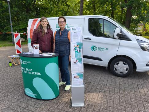 Petra (links) steht mit Frau Surhoff (rechts) am Info-Stand vor dem Info-Mobil. Die beiden posieren in die Kamera.
