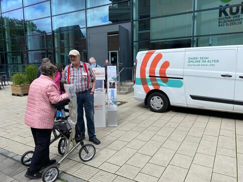 Eine &auml;ltere Frau mit Rollator steht mit einem Seniortrainer am Info-Stand neben dem Info-Mobil. Die beiden sind in einem Gespr&auml;ch.