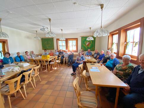 Im Sch&uuml;tzenheim in Schmidm&uuml;hlen sitzen an den W&auml;nden auf Sitzb&auml;nken insgesamt 22 Senior:innen und blicken in die Kamera. Das Bild ist im Weitwinkelmodus, damit alle Teilnehmende rauspassen,