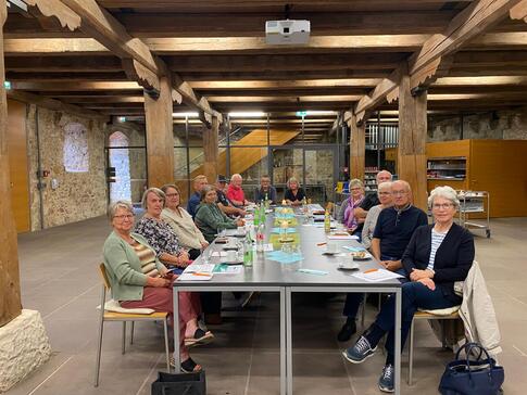 In einem Tagungsraum innerhalb der Burg Dagestein sitzen 16 Personen an einem langen Tisch. Sie blicken in die Kamera. Auf dem langen Tischen liegen Zettel und Brosch&uuml;ren.