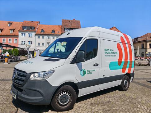 Das Infomobil steht auf einem gepflasterten Platz mit H&auml;usern im Hintergrund.