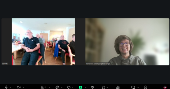 Bildschirmfoto vom Zoom-Fenster, in dem links die Teilnehmenden im Raum sitzend zu sehen sind und rechts Referent Johannes l&auml;chelnd in die Kamera blickt.
