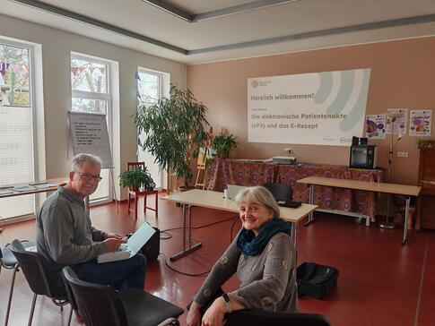 Ein Herr und eine Dame sitzen auf St&uuml;hlen und drehen sich und blicken in Richtung Kamera. 
