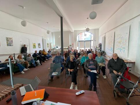 Im Stadthaus in Hessisch Oldendorf (ein gro&szlig;er Raum) sitzen auf mehreren Stuhlreihen und an der Seite Menschen zwischen 50 und 90 Jahren.