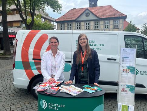 Mobilreferentin Petra (rechts) steht mit Frau Keese (links) am Info-Stand vor dem Info-Mobil. Beide posieren in die Kamera.