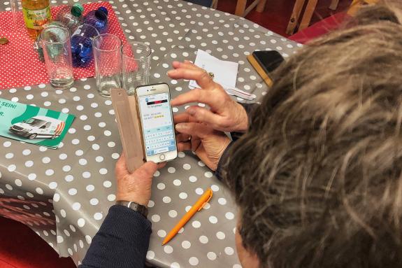 Eine Seniorin sitzt am Tisch und h&auml;lt ein Smartphone in der Hand