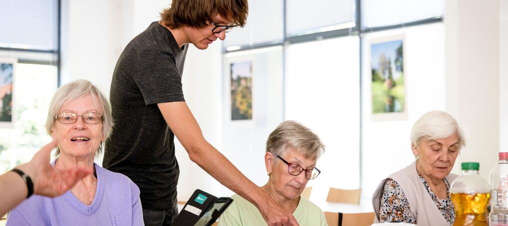 Junger Mann zeigt auf Smartphone einer &auml;lteren Frau. 